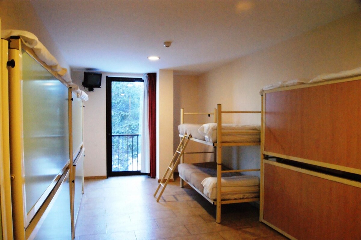 A dormitory room with bunk beds, a wooden wardrobe, a whiteboard, and a television.