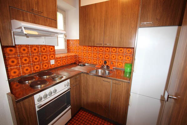 A compact kitchen with wooden cabinets, a gas stove, a sink, and a white refrigerator. - Chalet Cuore delle Alpi (Airolo)