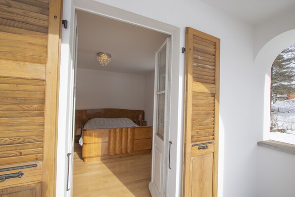 A bedroom with a wooden bed, a window with a view of snow outside, and a chandelier. - Chalet Cuore delle Alpi (Airolo)