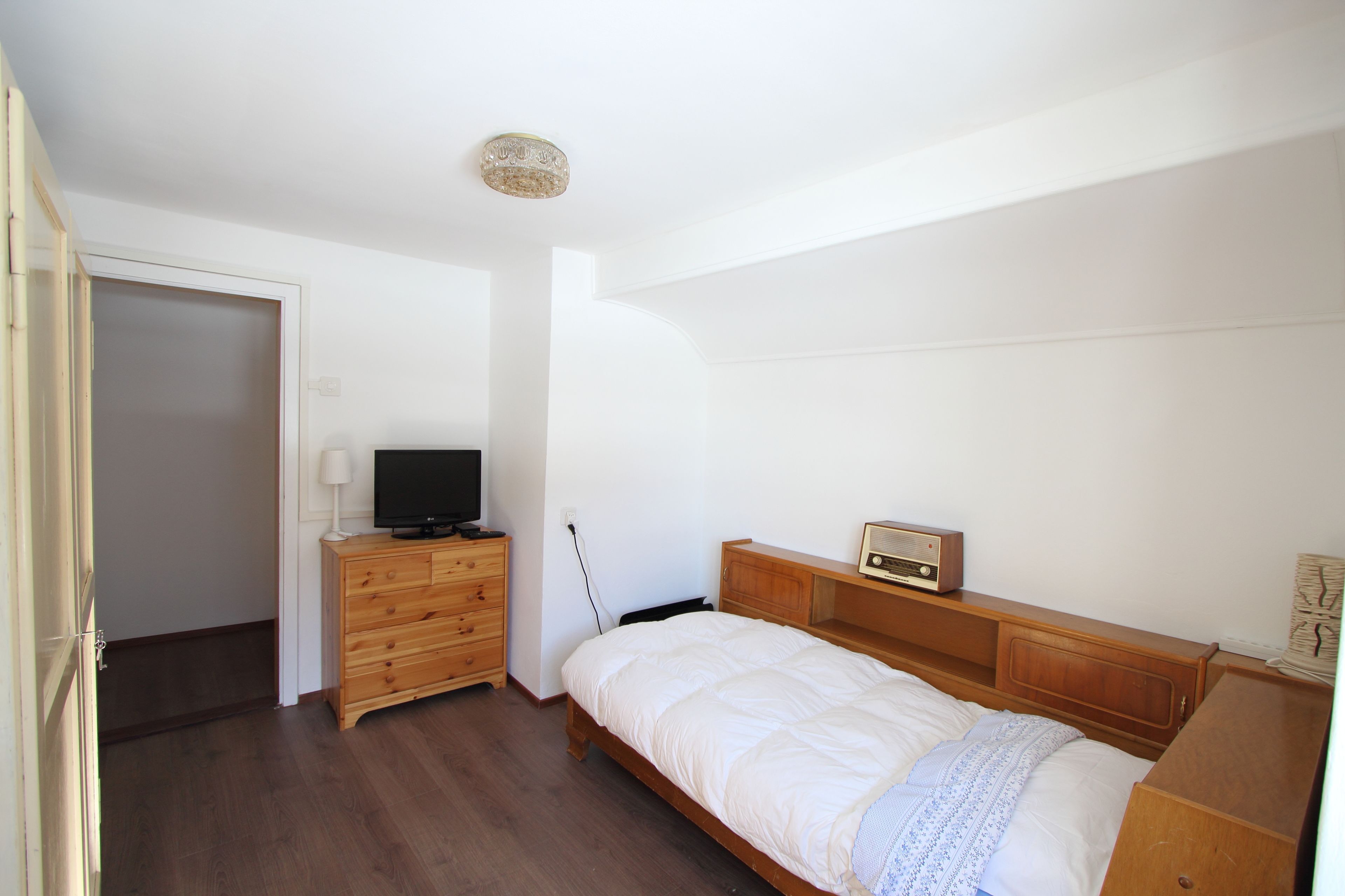 Une chambre à coucher avec un lit, une commode en bois, une télévision et une radio.