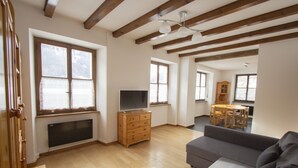 Un salón espacioso con piso de madera, un sofá gris, un aparador de madera y un televisor.