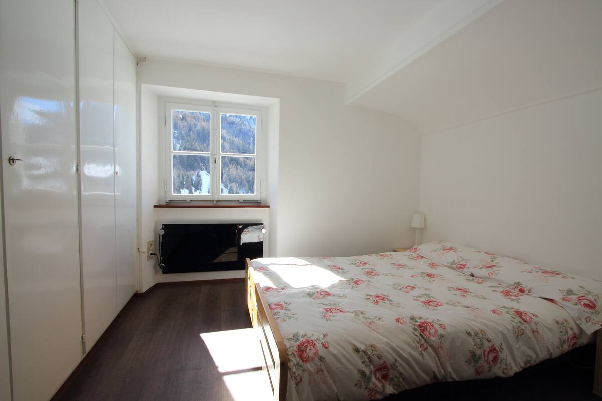 Een slaapkamer met een bed, een raam, een bureau en een kledingkast.
