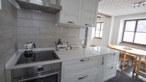 Una cocina moderna con armarios blancos, estufa empotrada y un comedor con mesa y sillas de madera.