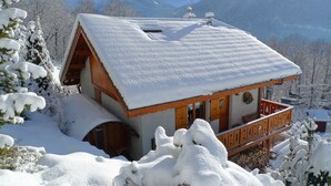 Eine Holzhütte mit verschneitem Dach vor einer Bergkulisse.