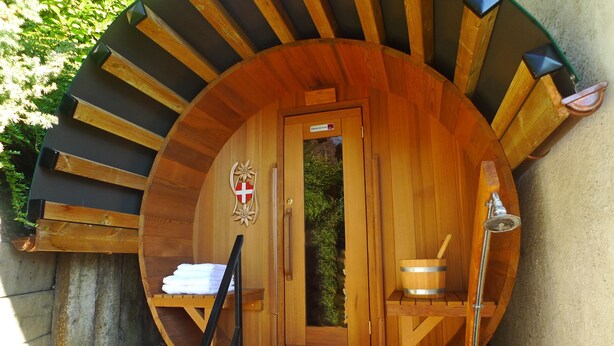 Eine finnische Holzsauna mit kreisförmigem Design, einer Tür, einem Handtuchhalter, einem Eimer und einem Handtuch.