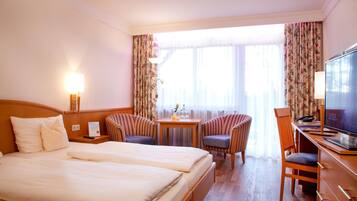 A hotel room with a double bed, two armchairs, a desk with a television, and a small table with a lamp.