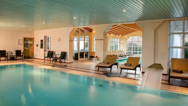 Una gran piscina interior con sillones de descanso y techo de madera.