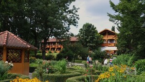Un jardín con un pabellón, setos recortados y un edificio con balcones.