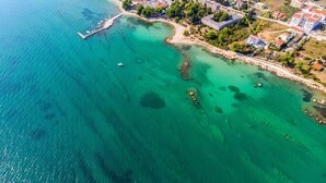 Ein Luftbild einer Küstenlandschaft mit klarem türkisblauem Wasser, einem Steg und Wohngebäuden mit roten Dächern.
