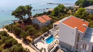Ein modernes, zweistöckiges Haus mit Swimmingpool, umgeben von Bäumen und mit Blick auf ein ruhiges Meer.