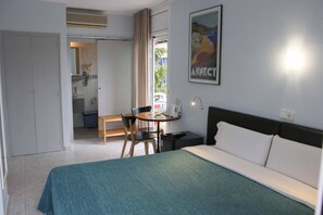A hotel room with a bed, a desk, a chair, a small table, and a window with curtains. - Hotel Alexandra Sitges (Sitges)