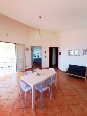 Un espace repas comprenant une table et des chaises, un canapé, un luminaire au plafond et une porte donnant sur une autre pièce.