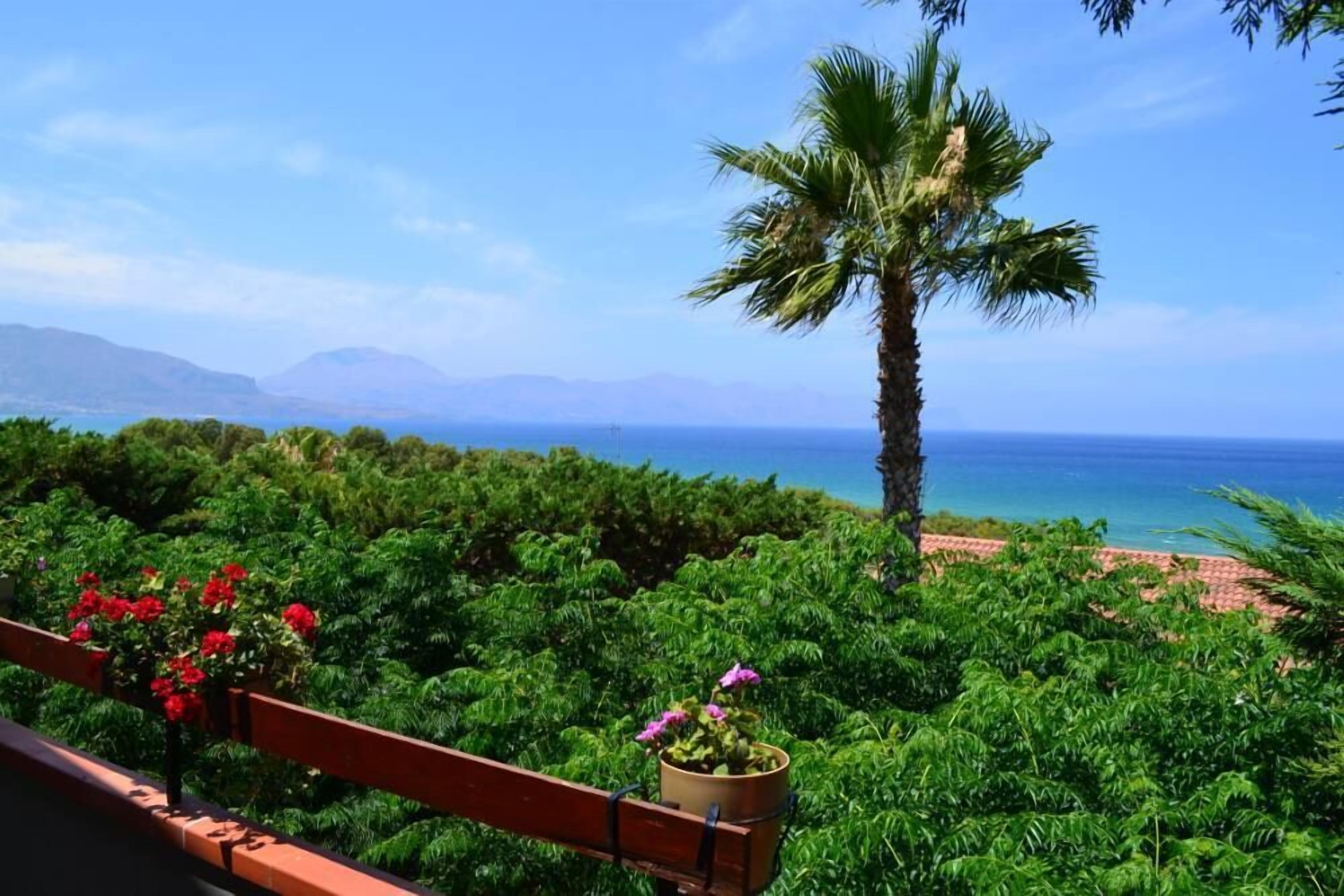 A balcony with lush greenery and a view of the ocean.