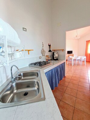 Una cocina moderna con un lavamanos de acero inoxidable, una estufa a gas y un comedor con sillas blancas y una mesa.