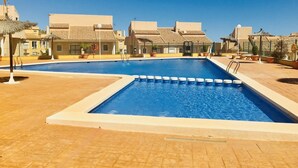 Una piscina con agua cristalina azul, rodeada de edificios con tejas y un estilo arquitectónico uniforme.