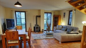 A living room with a sofa, TV, wooden dining table, chairs, and a fireplace. - Vacation home close to the beach with sauna incl. additional costs, home office possible (Glowe)