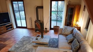 A living room with a sofa, a coffee table, a TV, and a fireplace. - Vacation home close to the beach with sauna incl. additional costs, home office possible (Glowe)