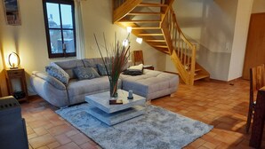 A living room with a wooden staircase, a sofa, a coffee table, and a rug. - Vacation home close to the beach with sauna incl. additional costs, home office possible (Glowe)