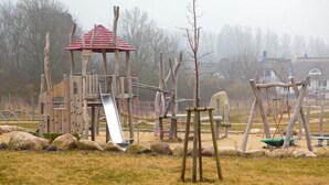 A playground with a slide, swings, and a climbing structure. - Vacation home close to the beach with sauna incl. additional costs, home office possible (Glowe)