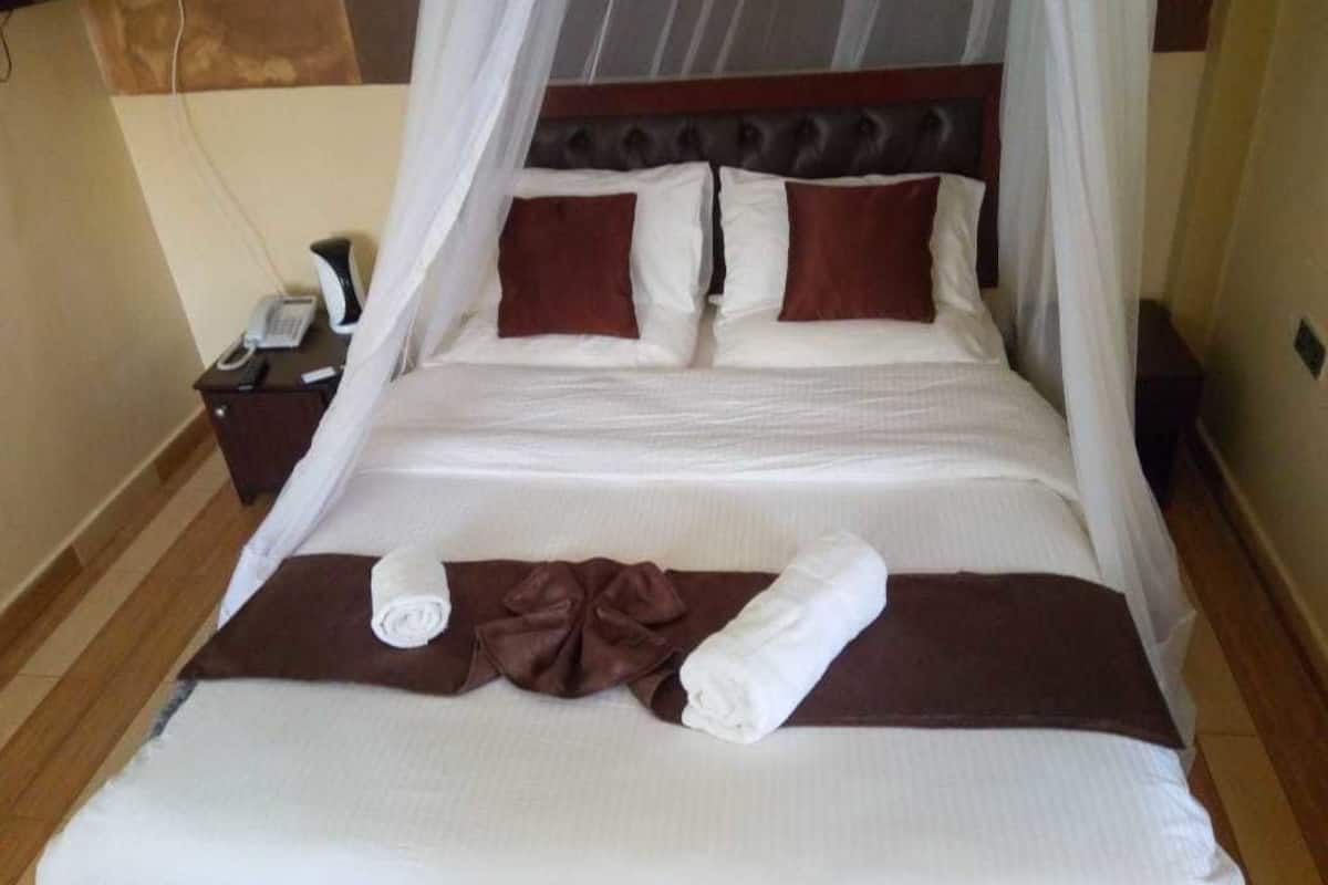 A neatly made bed with a brown and white color scheme, a telephone on the nightstand, and a wall-mounted TV.