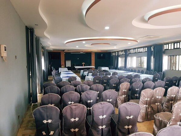 Una sala de conferències amb files de cadires, una taula llarga i un escenari.