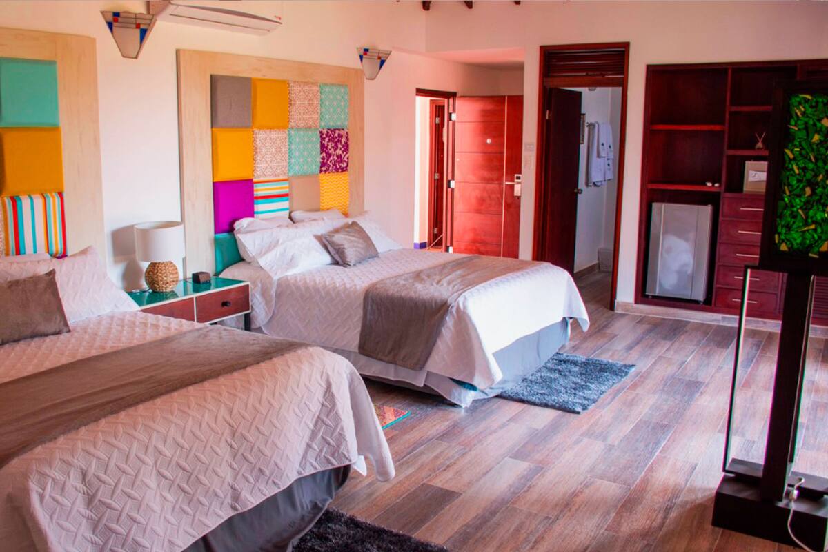A hotel room with two beds, a colorful wall art, a wooden floor, and a wardrobe.