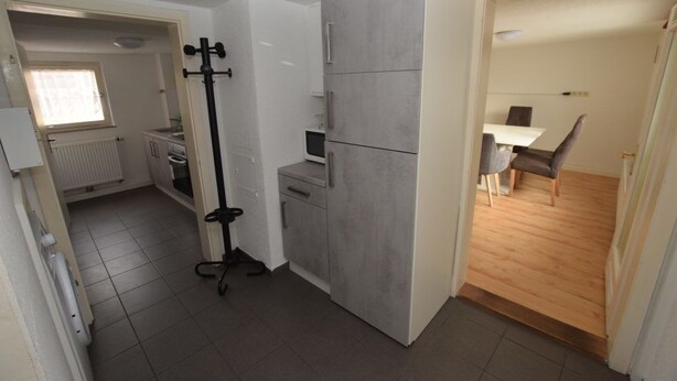 Una cocina compacta con armarios grises, un batidor negro y un área de comedor con mesa y sillas.