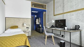 Una habitación de hotel con cama, escritorio, silla y un pequeño cubo de basura.