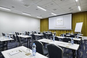 Un salón de conferencias con mesas, sillas, botellas de agua y una pantalla para presentaciones al frente.