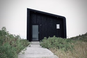 A modern black building with a single door and a small window, surrounded by natural vegetation. - iStay Cottages (Suðurnesjabær)