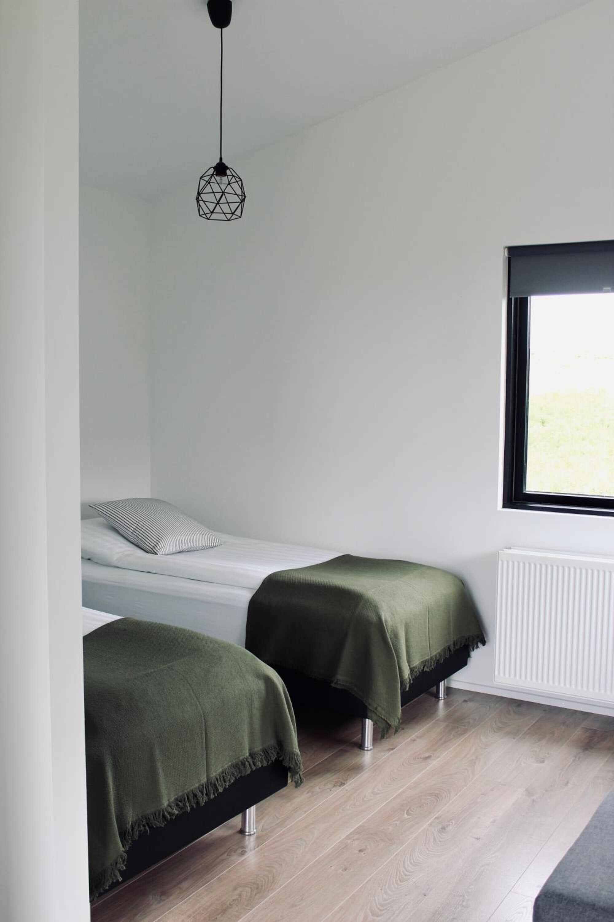 A minimalist room with two single beds, a window with a view, and a hanging light fixture.