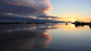 A calm waterfront at sunset with boats docked, a pier, and a calm sea reflecting the sky.