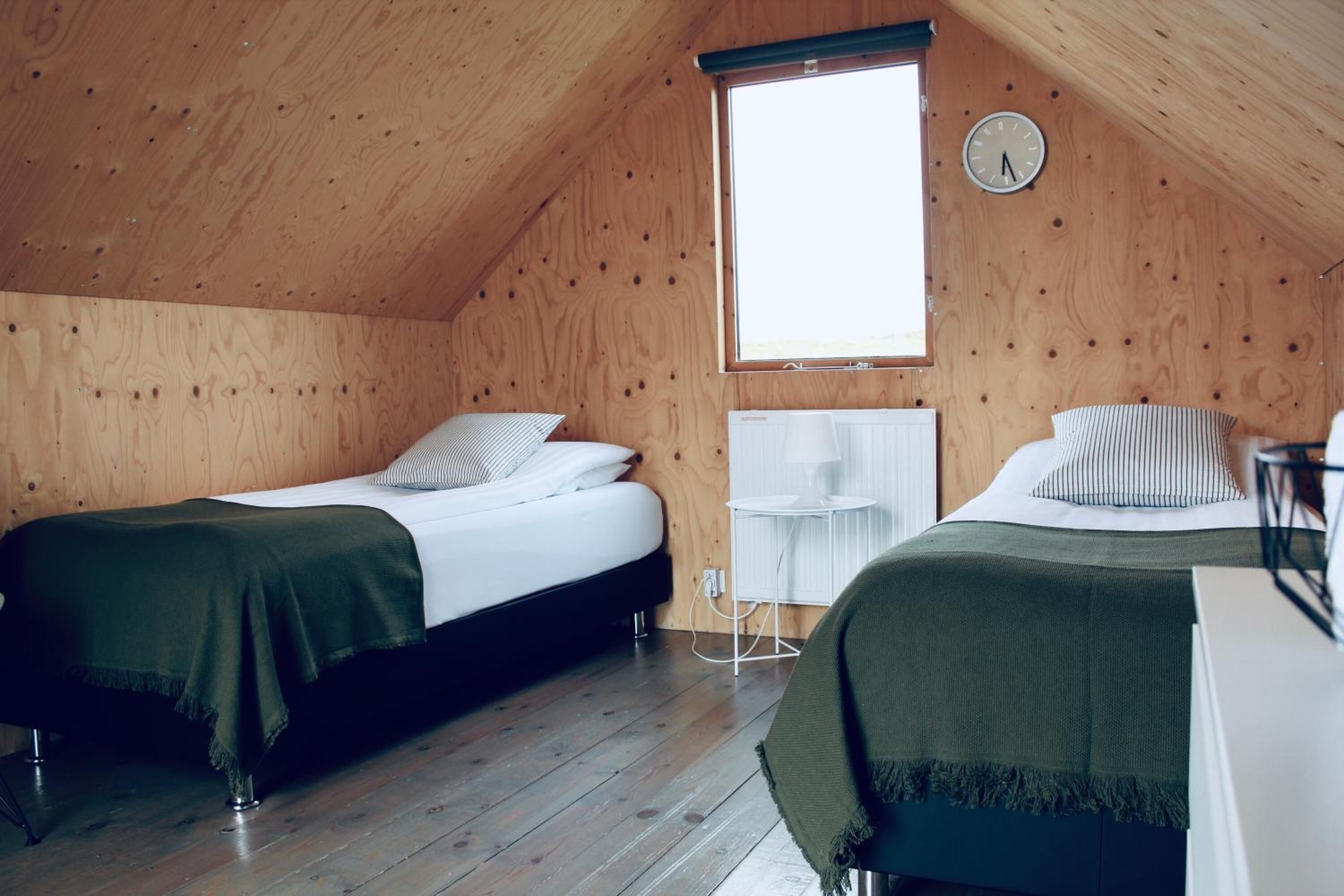 A cozy attic bedroom with two beds, wooden walls, a window, and a white radiator.