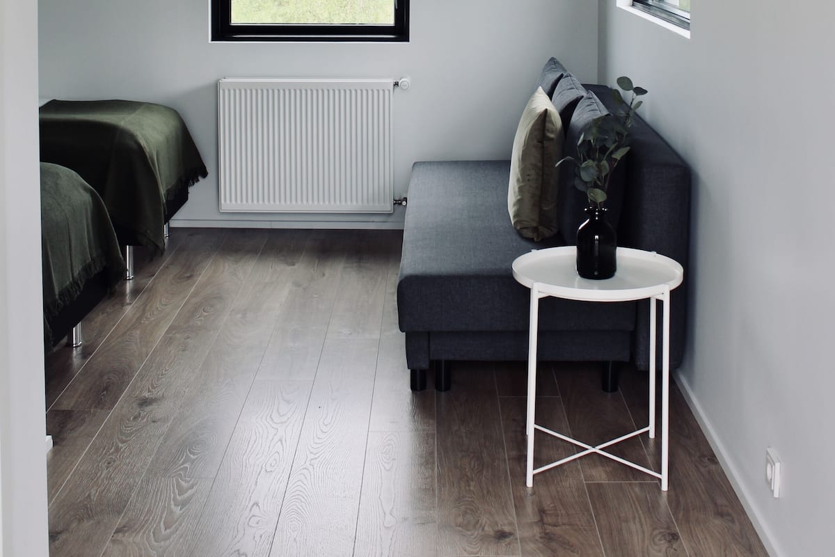 A room with a window, a radiator, a sofa, a small table, and a TV mounted on the wall.