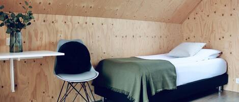 A small, wooden-paneled room with a bed, a desk, and a chair.