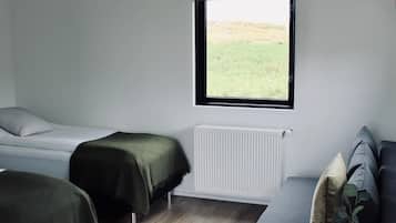 A bedroom with two beds, a window with a view, a radiator, and a small table with a vase.