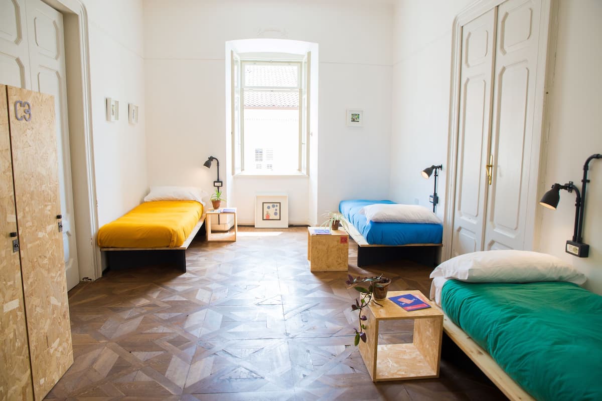 Una habitación con dos camas, piso de madera, una ventana y una puerta.