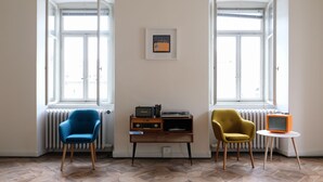 A room with two large windows, a radiator, a small wooden table, and two chairs. - ControVento (Trieste)