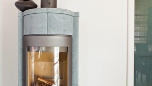 Ein moderner Holzofen mit Glasfront, grauem Gehäuse und schwarzem Schornstein.
