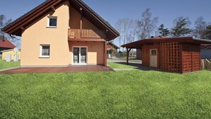 Ein zweistöckiges Haus mit Balkon, einer Holzterrasse und einem umzäunten Bereich.