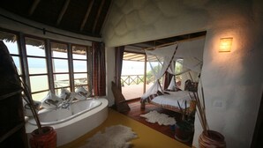 A bedroom with a large bathtub, a bed with a canopy, and a view of the beach. - Sunbird Lodge Elementaita (Nakuru)