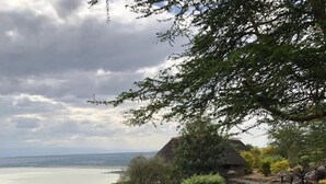 A stone pathway leading to a seating area with a view of the sea and a thatched-roof structure. - Sunbird Lodge Elementaita (Nakuru)
