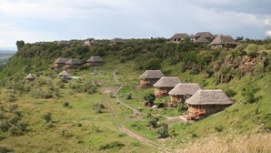 A series of thatched-roof huts arranged on a hillside, connected by a winding path. - Sunbird Lodge Elementaita (Nakuru)