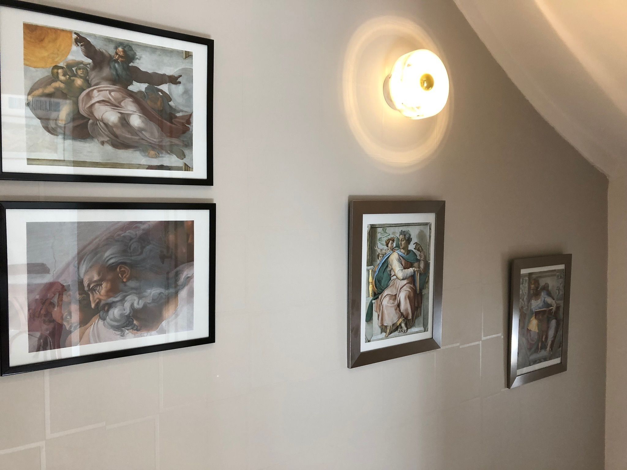A hallway with framed artwork on the walls, a light fixture, and a tiled floor.