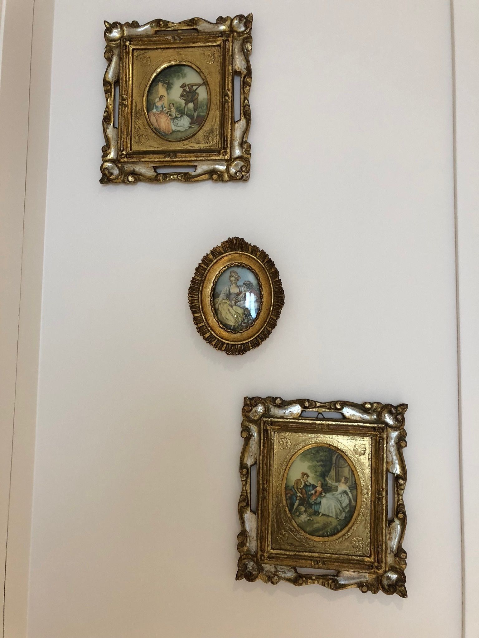 Tres cuadros decorativos con marcos dorados, sujetos a la pared, que representan escenas clásicas.