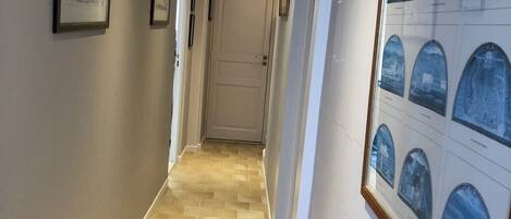A hallway with patterned floor tiles, framed artwork on the walls, and a door at the end.