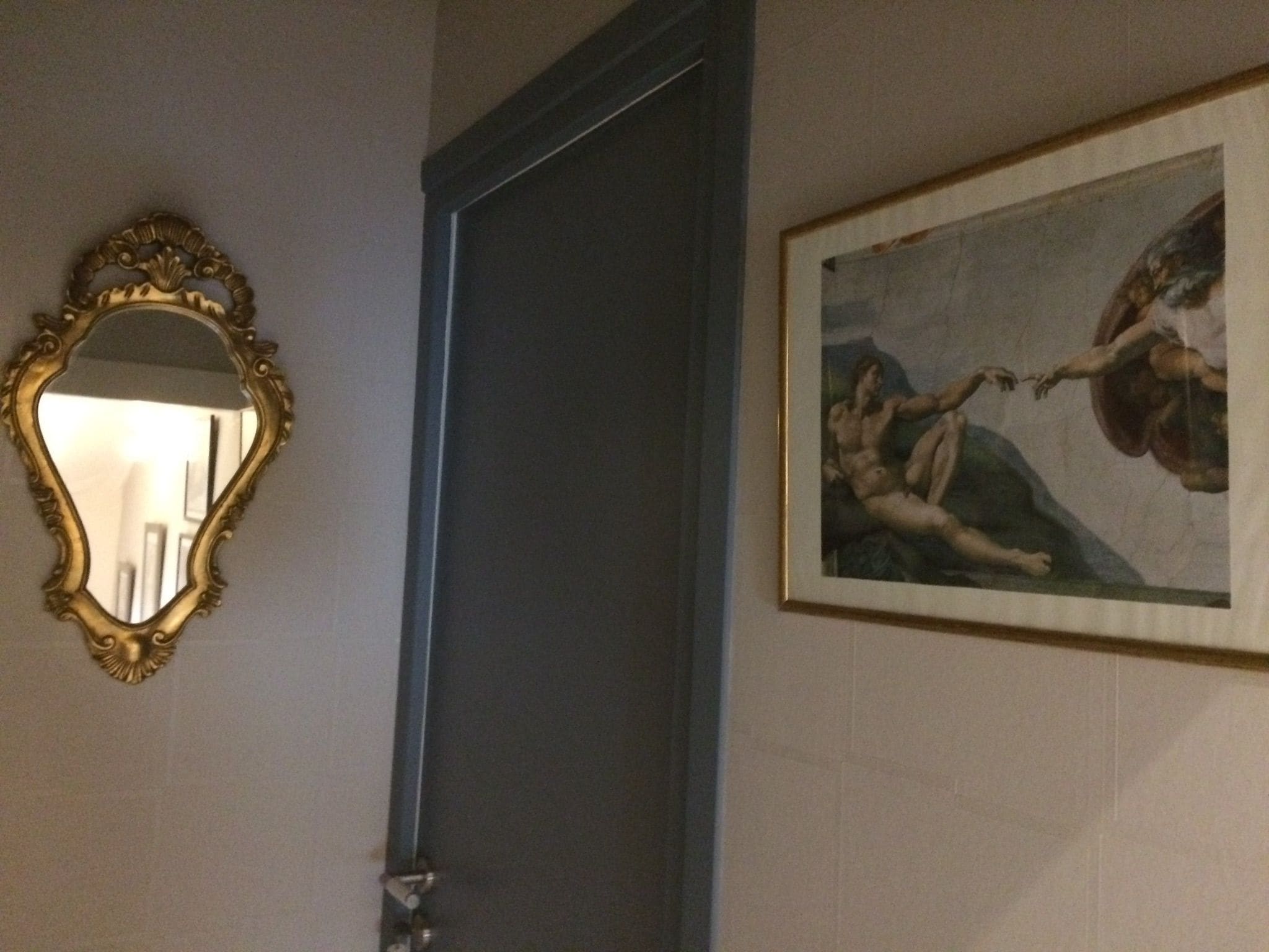 A mirror with an ornate gold frame, a door, and a classical painting on the wall.