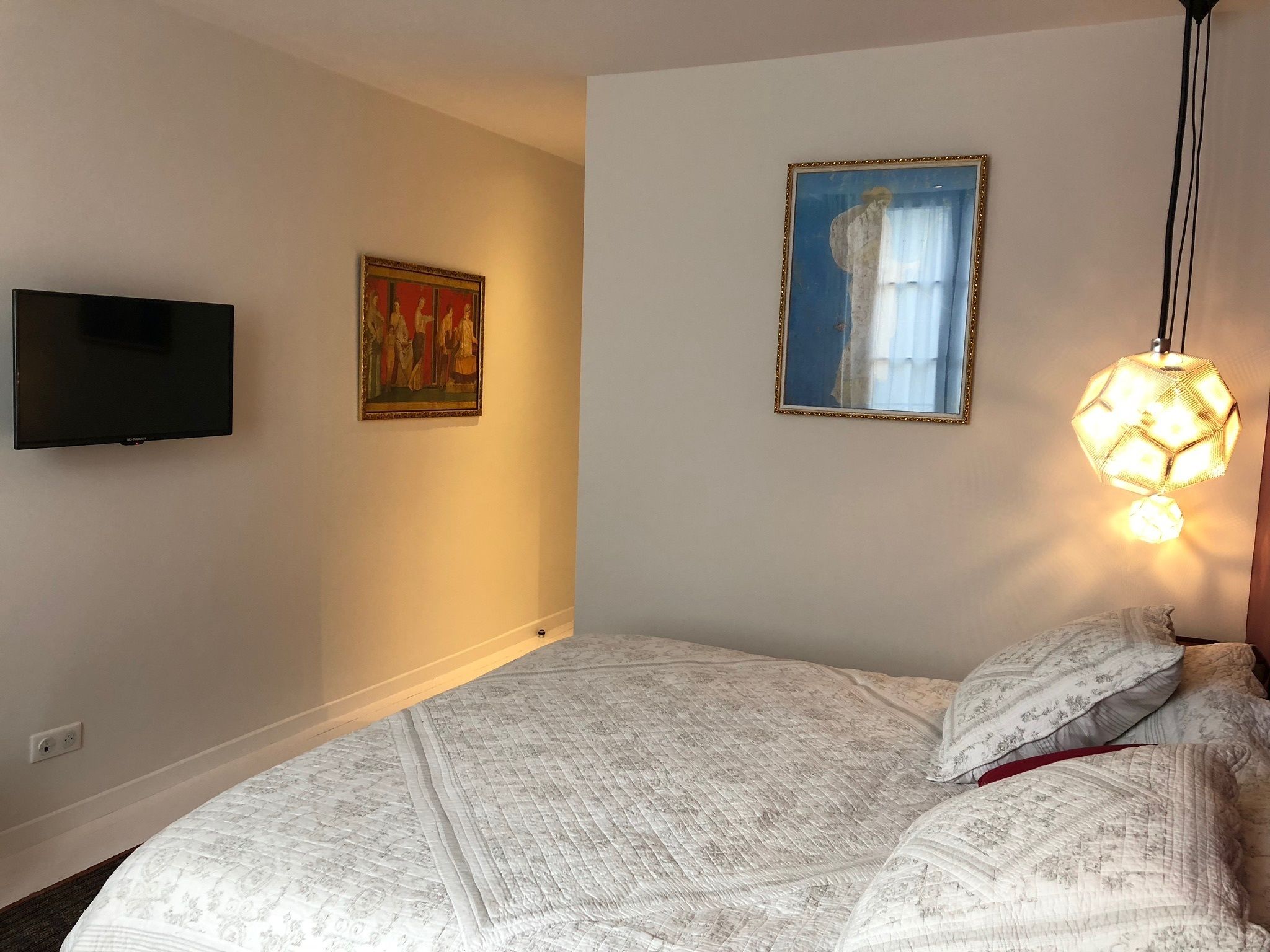 A bedroom with a bed, a television, and two framed artworks on the wall.