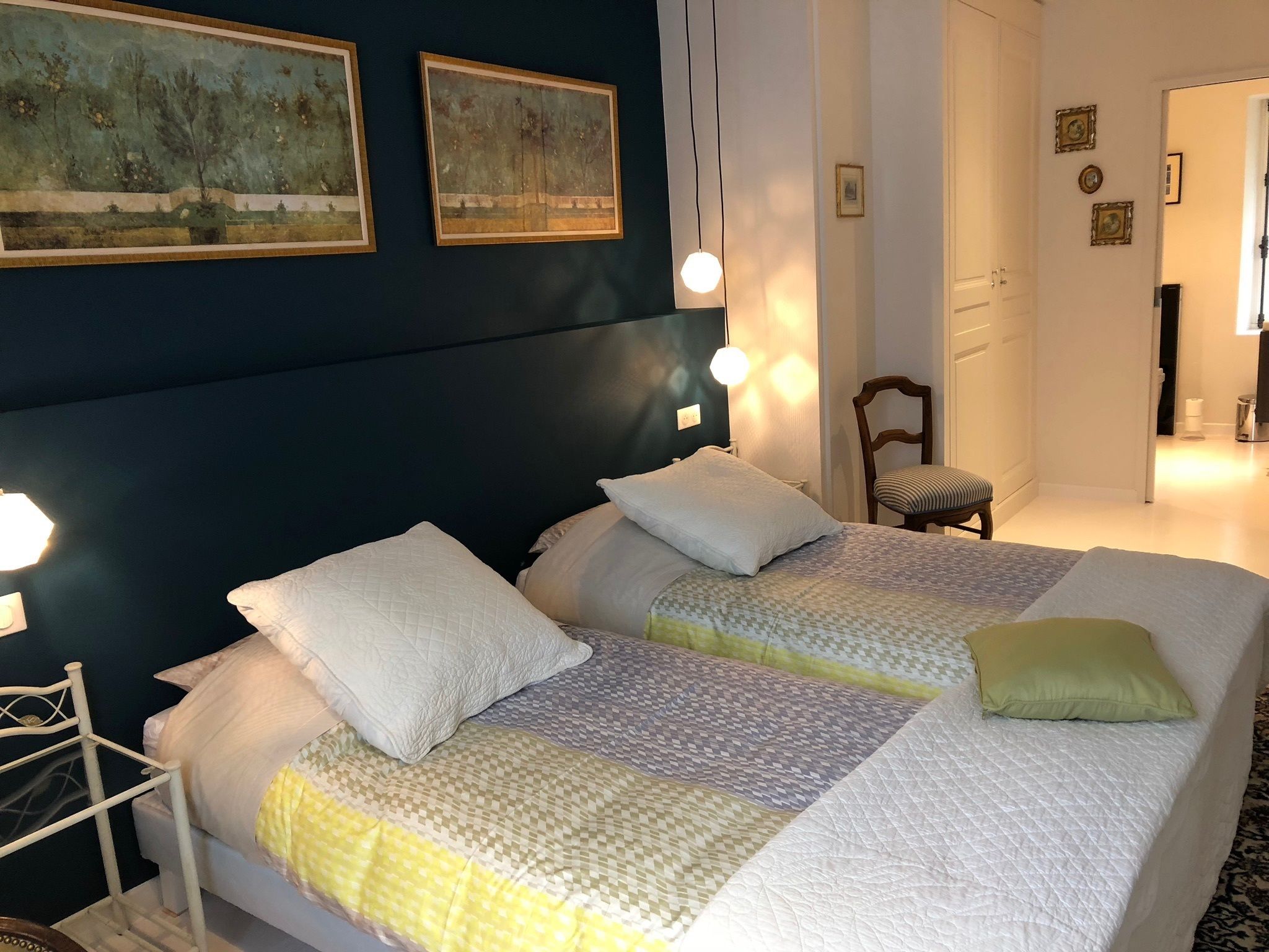 A bedroom with two beds, a chair, and artwork on the wall.