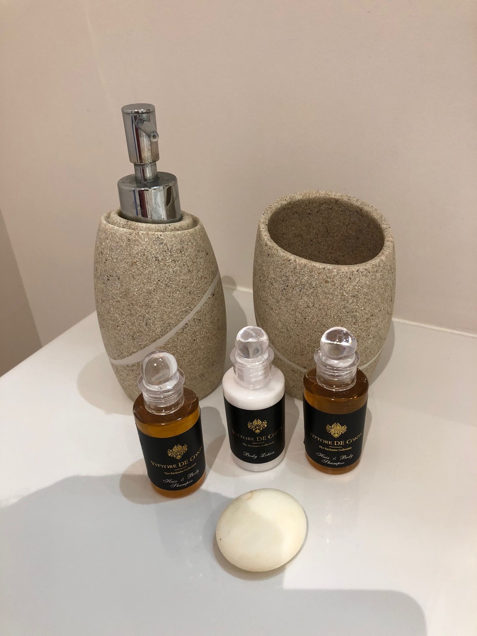 Ein Badezimmer mit einem Steintonne, einem Metallarmaturen und drei Flaschen Haarpflegeprodukten.